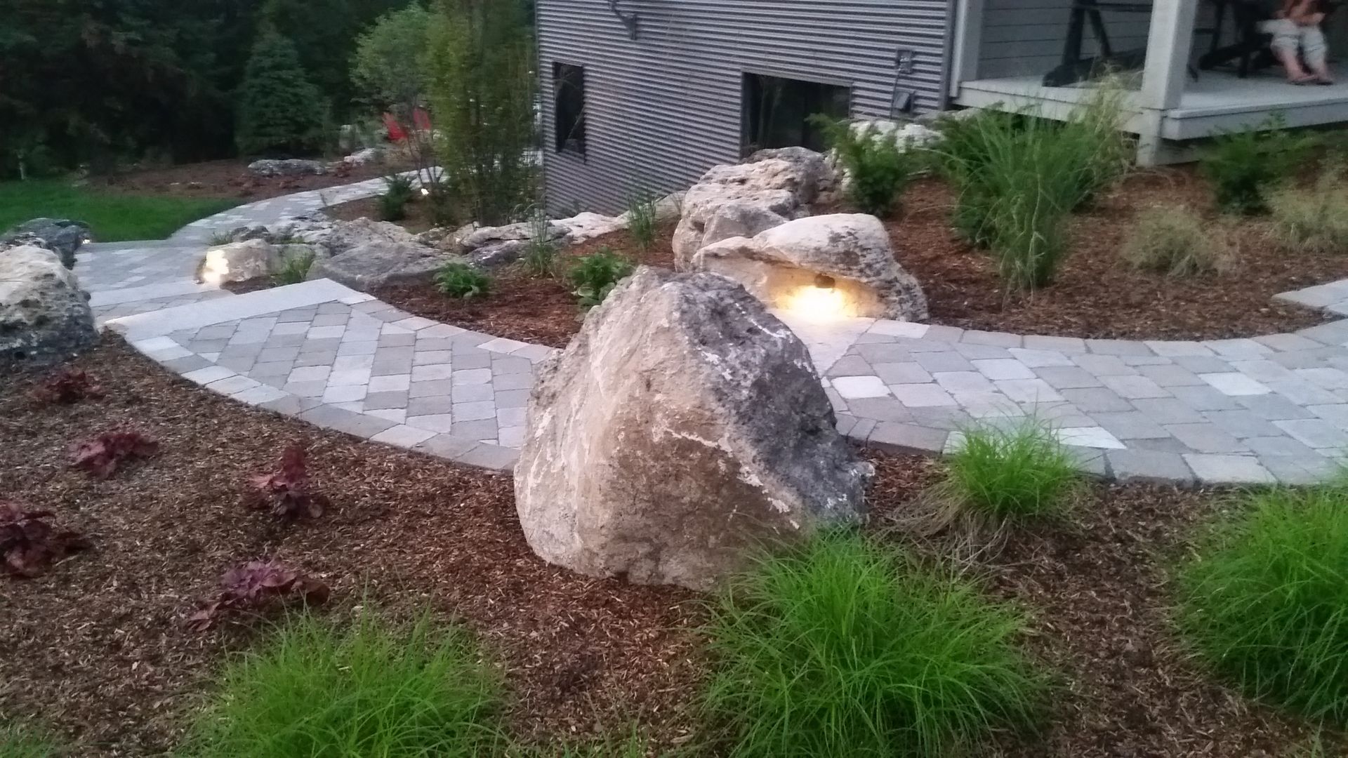 A large rock is sitting in the middle of a garden next to a walkway.