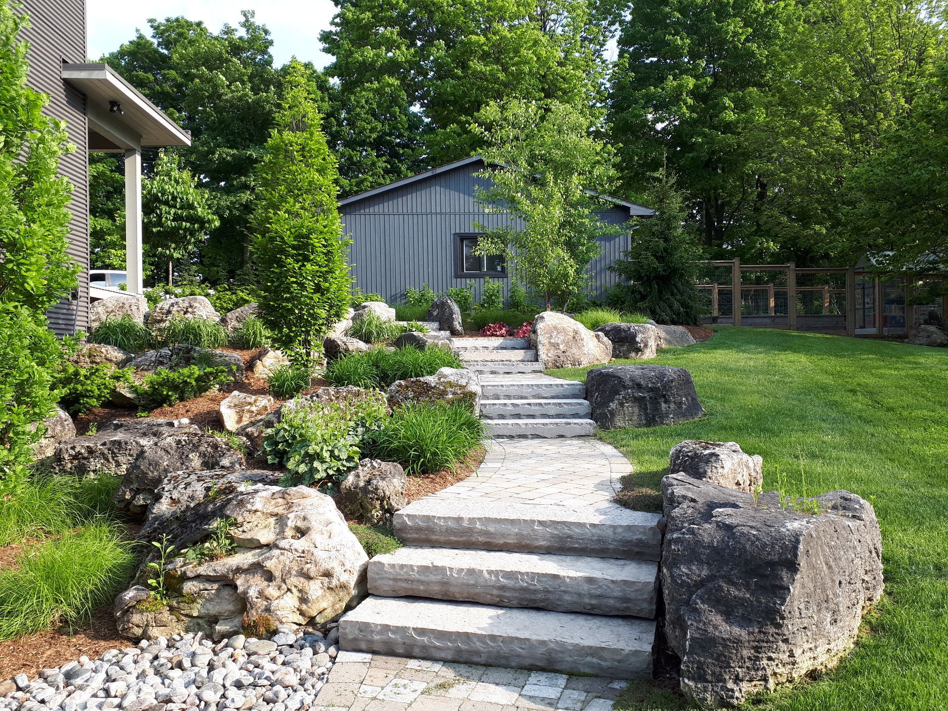 A stone walkway leading to a house surrounded by rocks and grass.