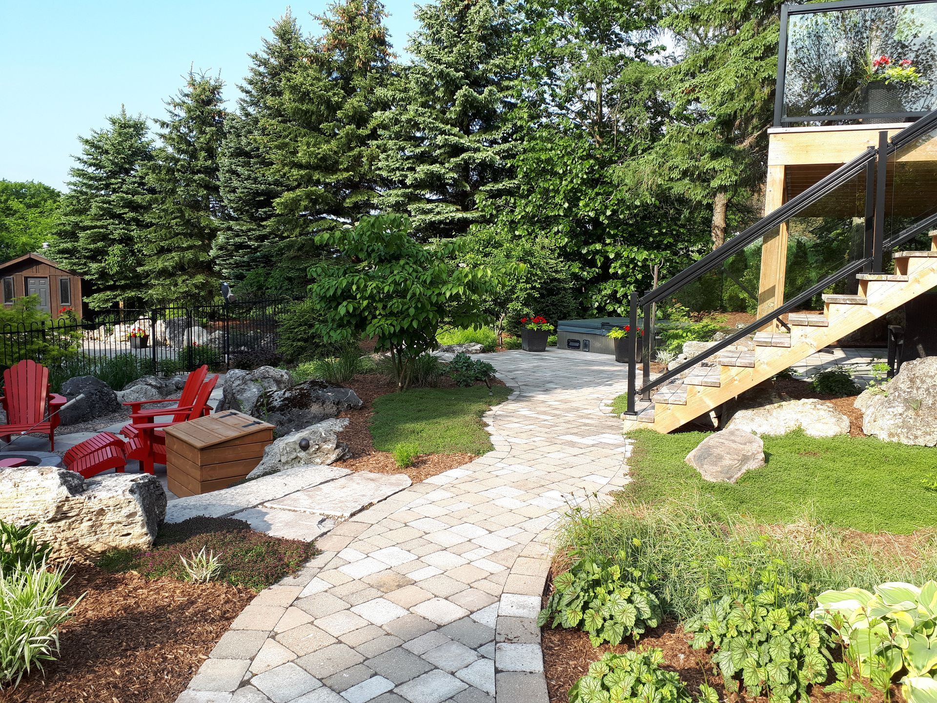 A brick walkway leading to a deck in a backyard surrounded by trees.