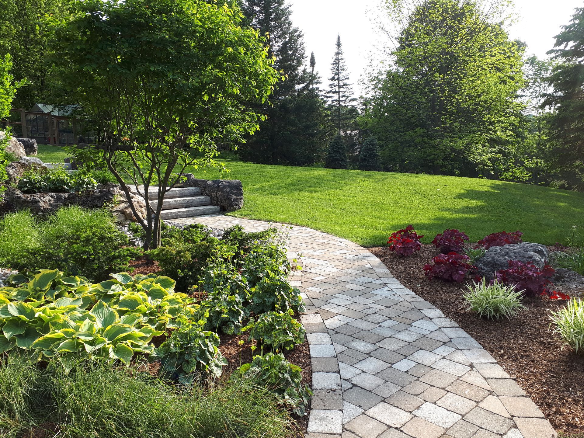 A brick walkway leading to a lush green field surrounded by trees and bushes.