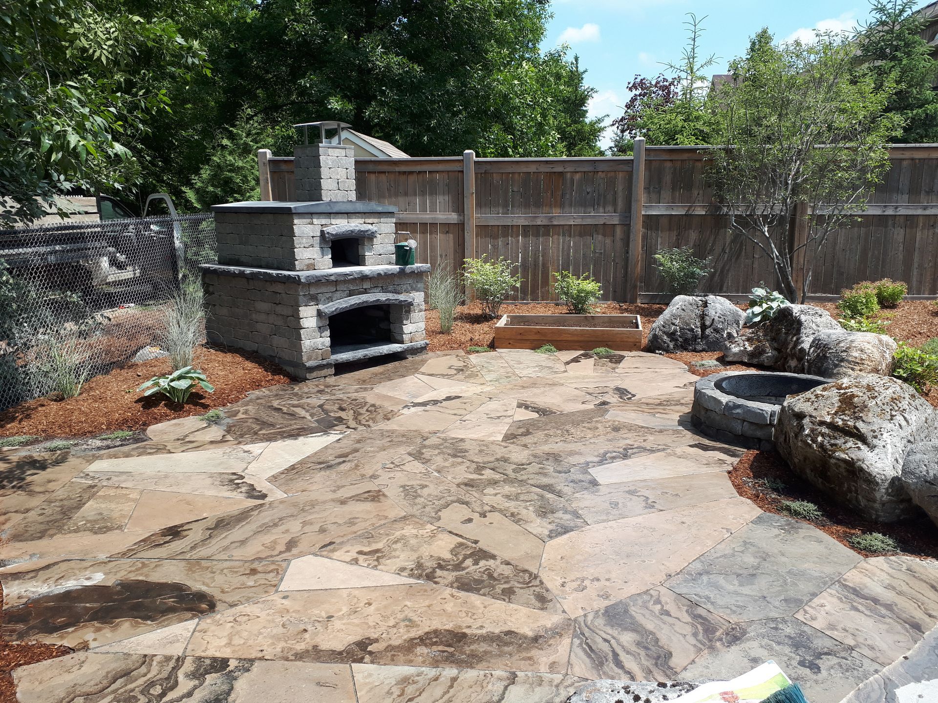 A patio with a pizza oven and a wooden fence in the background.