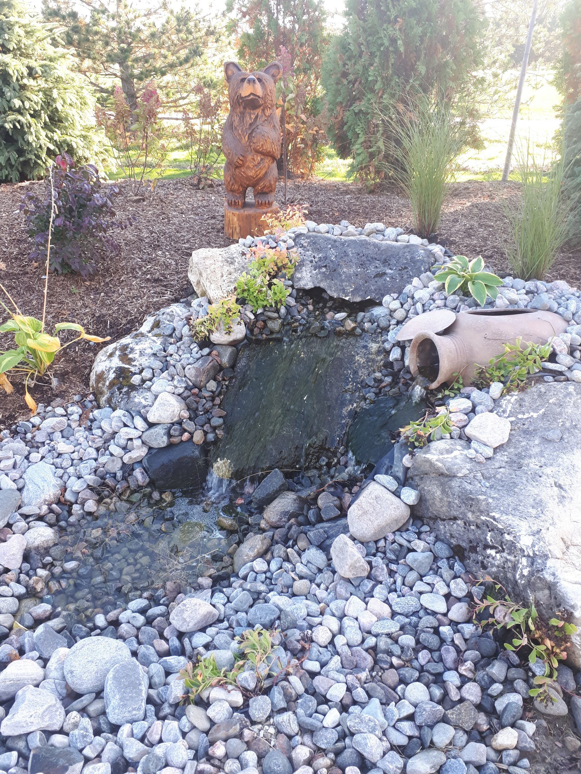 A small pond surrounded by rocks and a statue of a bear.