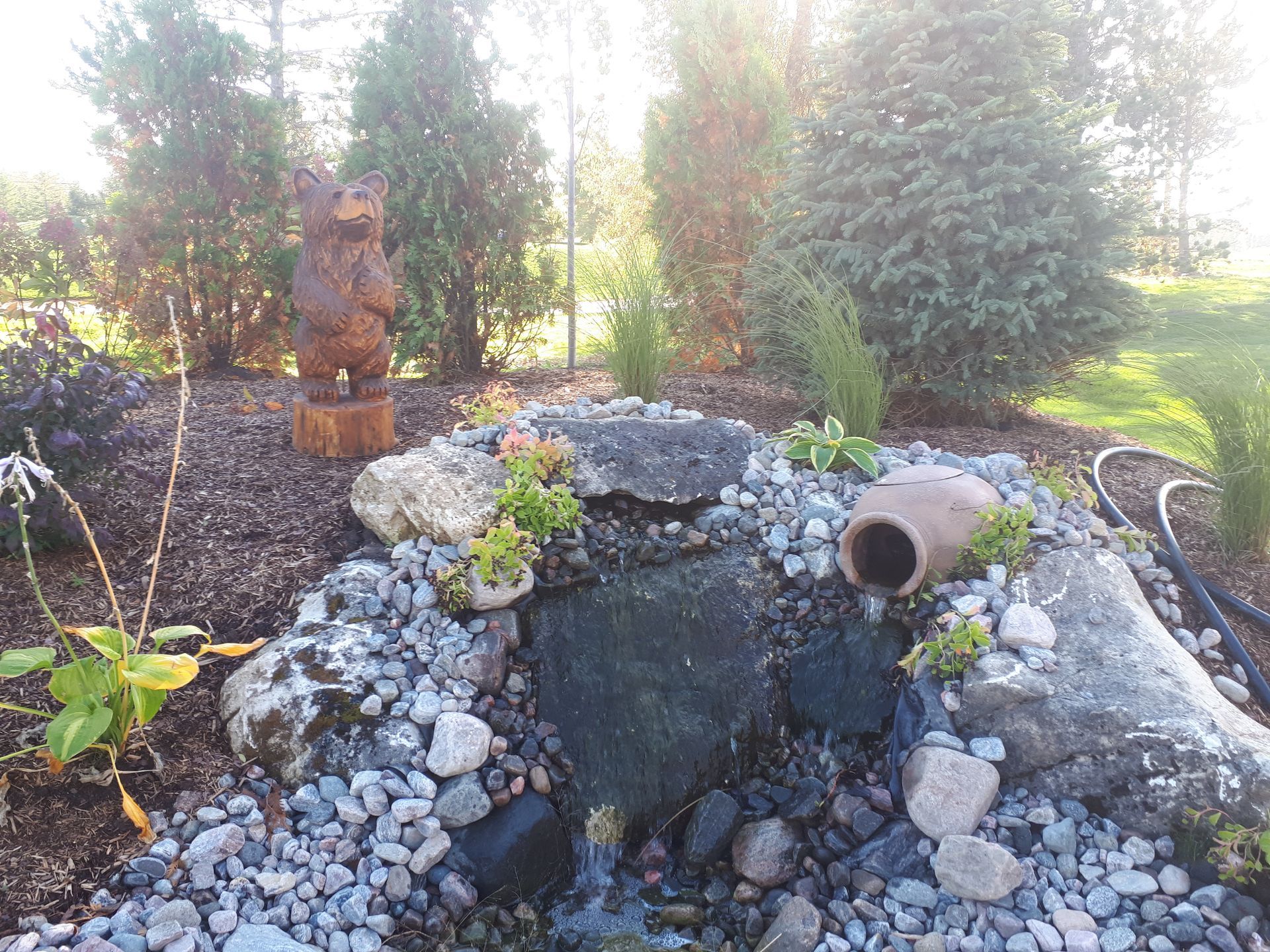 A small waterfall in a garden with a bear statue in the background.
