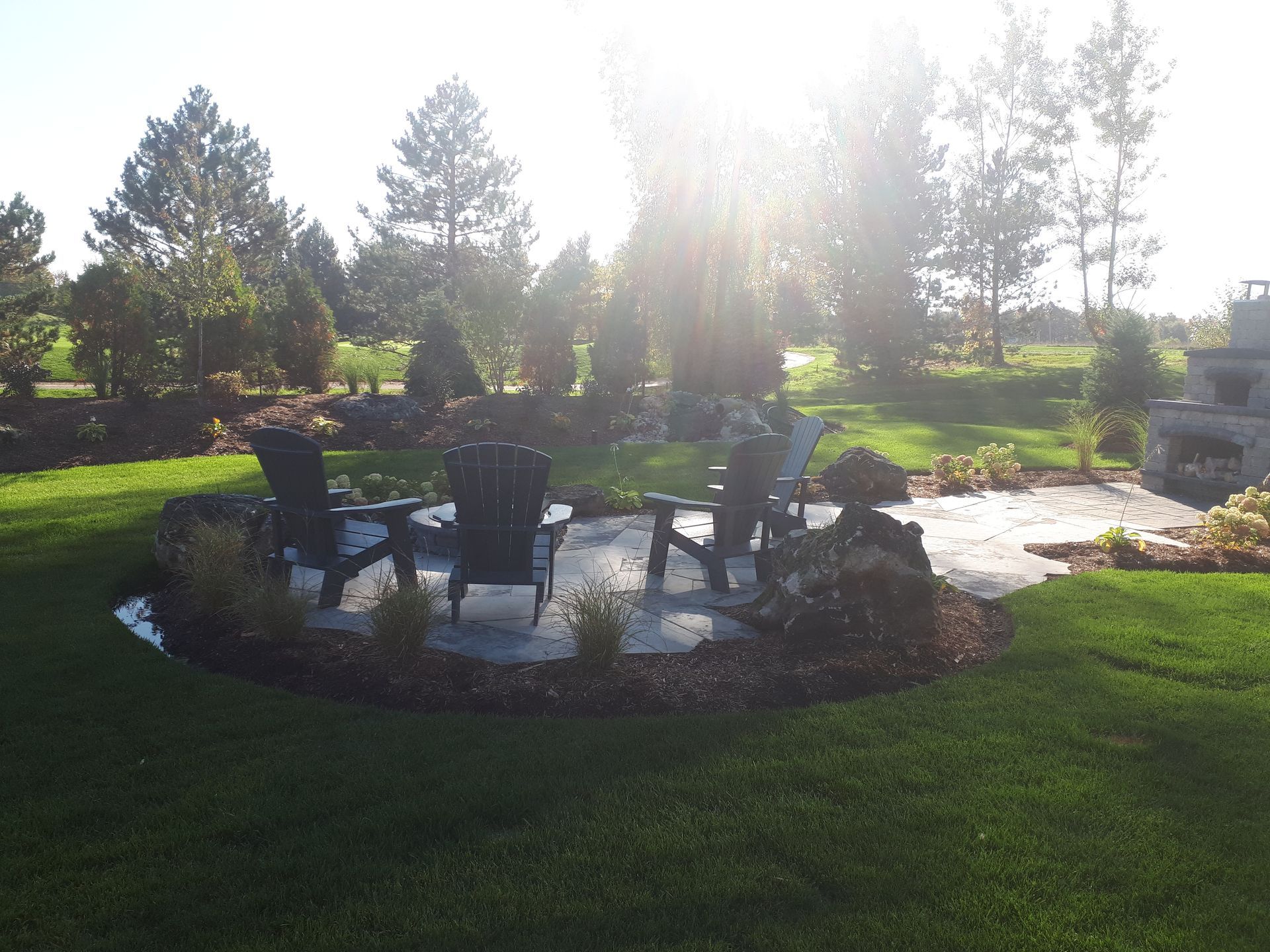 A patio with chairs and a table in the middle of a lush green field.
