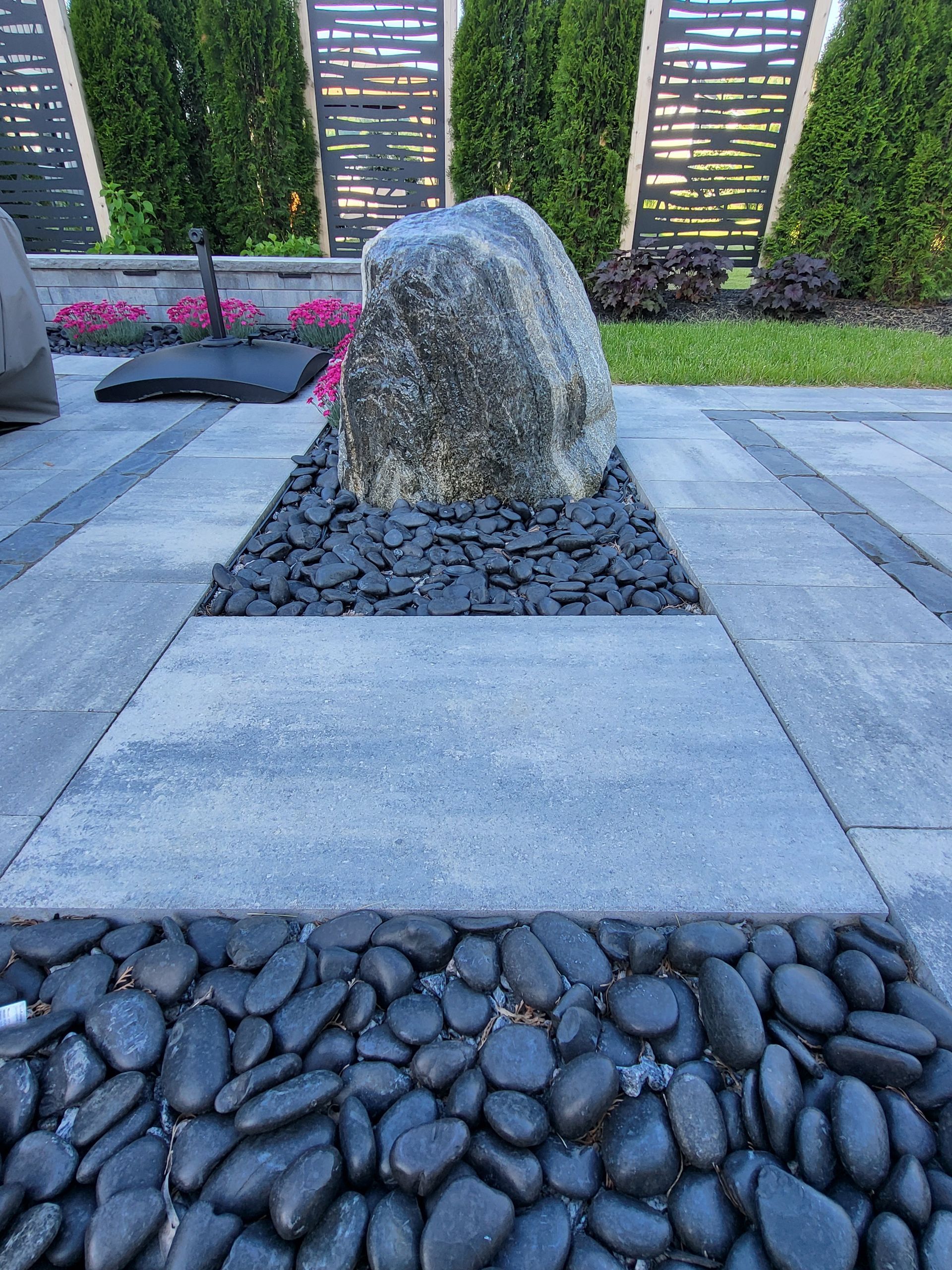 A large rock is surrounded by black rocks on a patio.