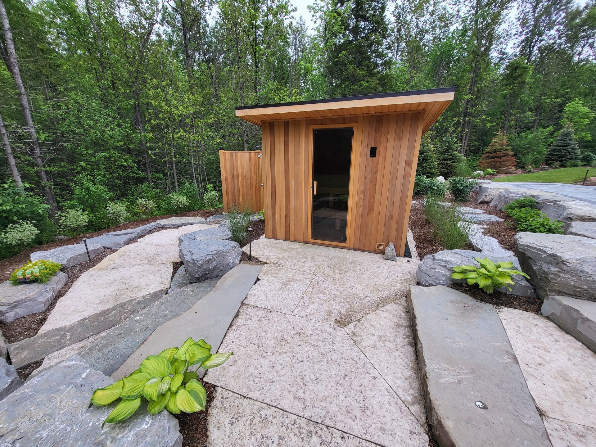 A small wooden sauna is surrounded by rocks and trees.