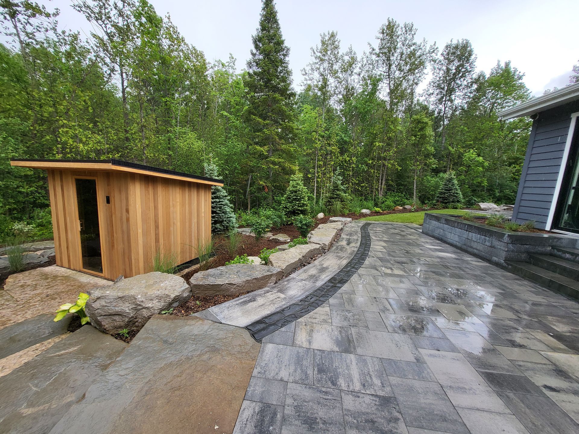 A wooden shed is sitting on top of a patio next to a house.