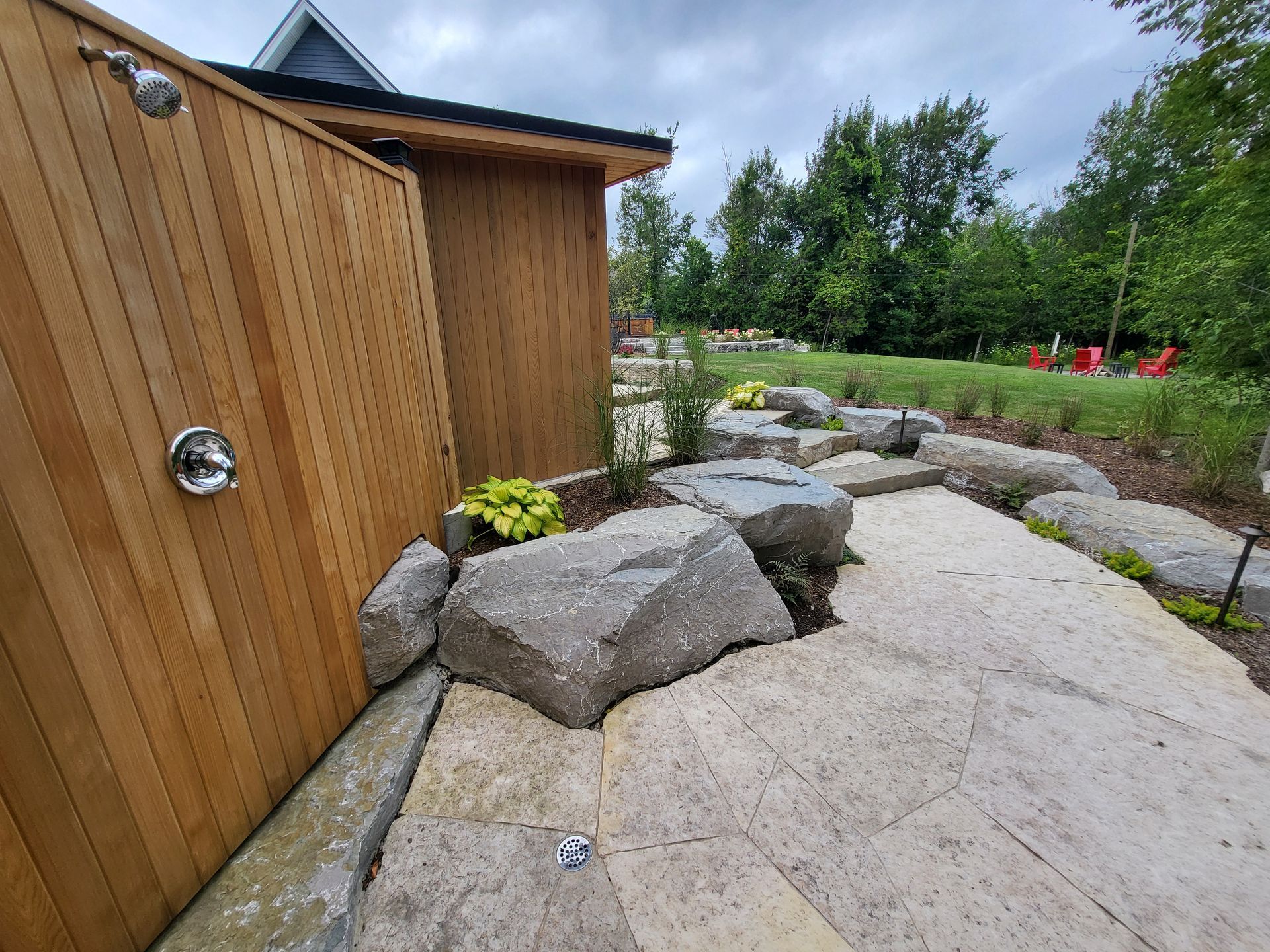 A wooden shower is surrounded by rocks and trees in a backyard.