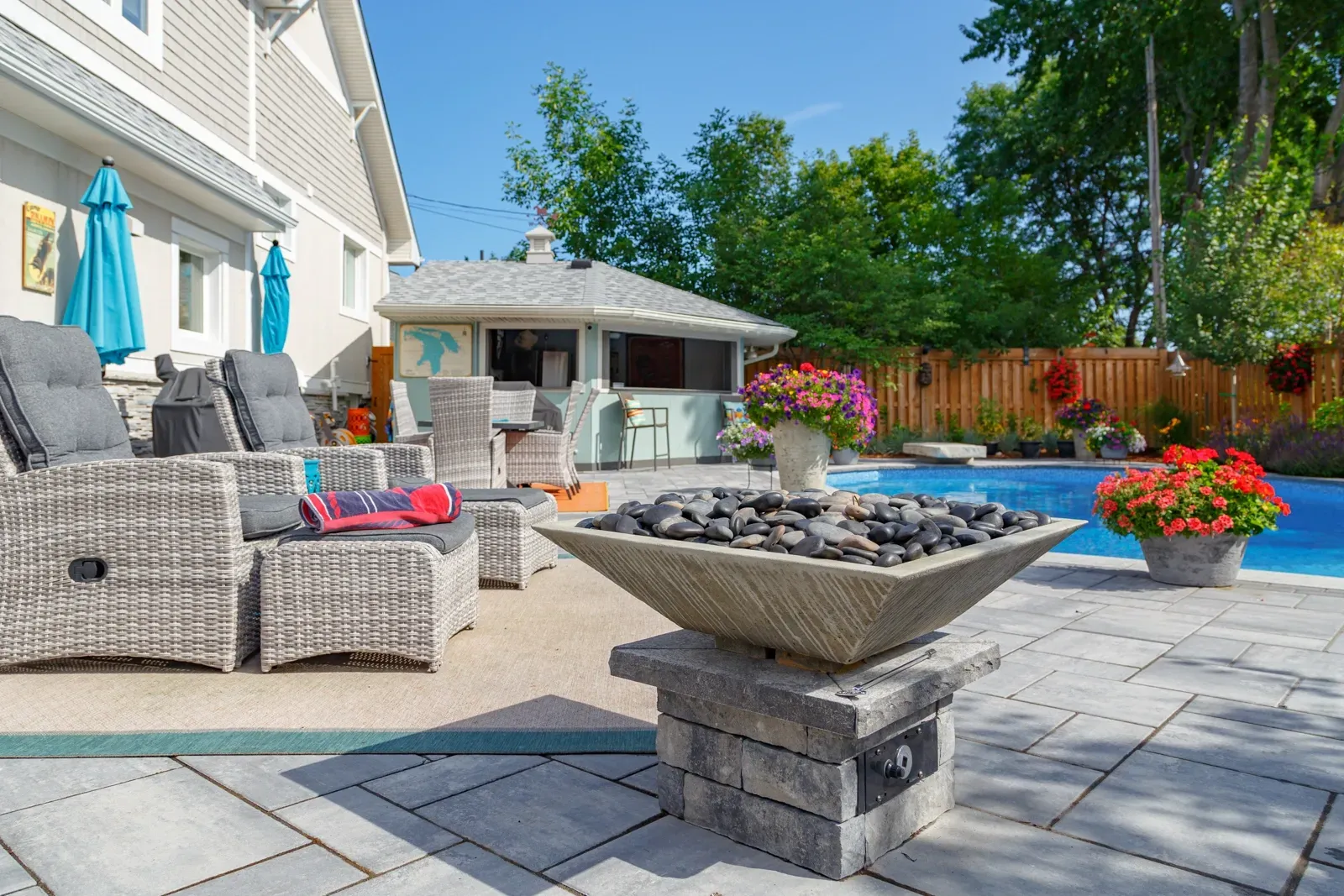 A fire pit is in the middle of a patio next to a pool.