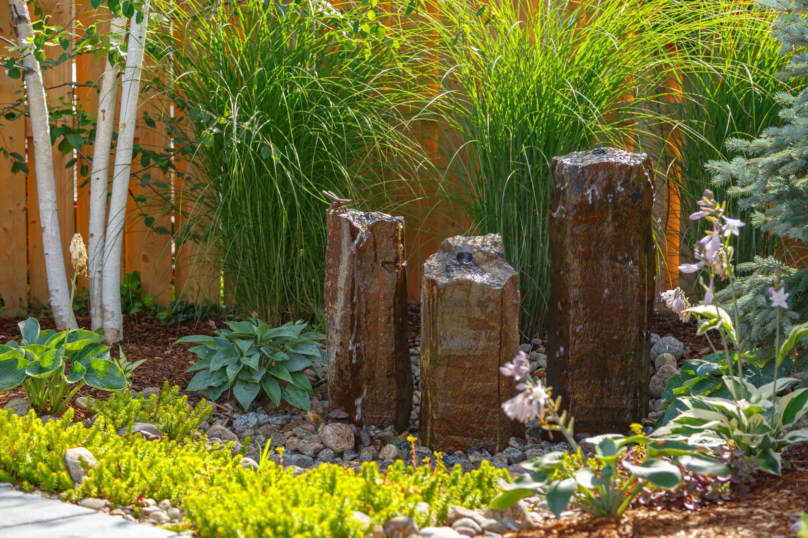 There is a fountain in the middle of the garden surrounded by plants and trees.