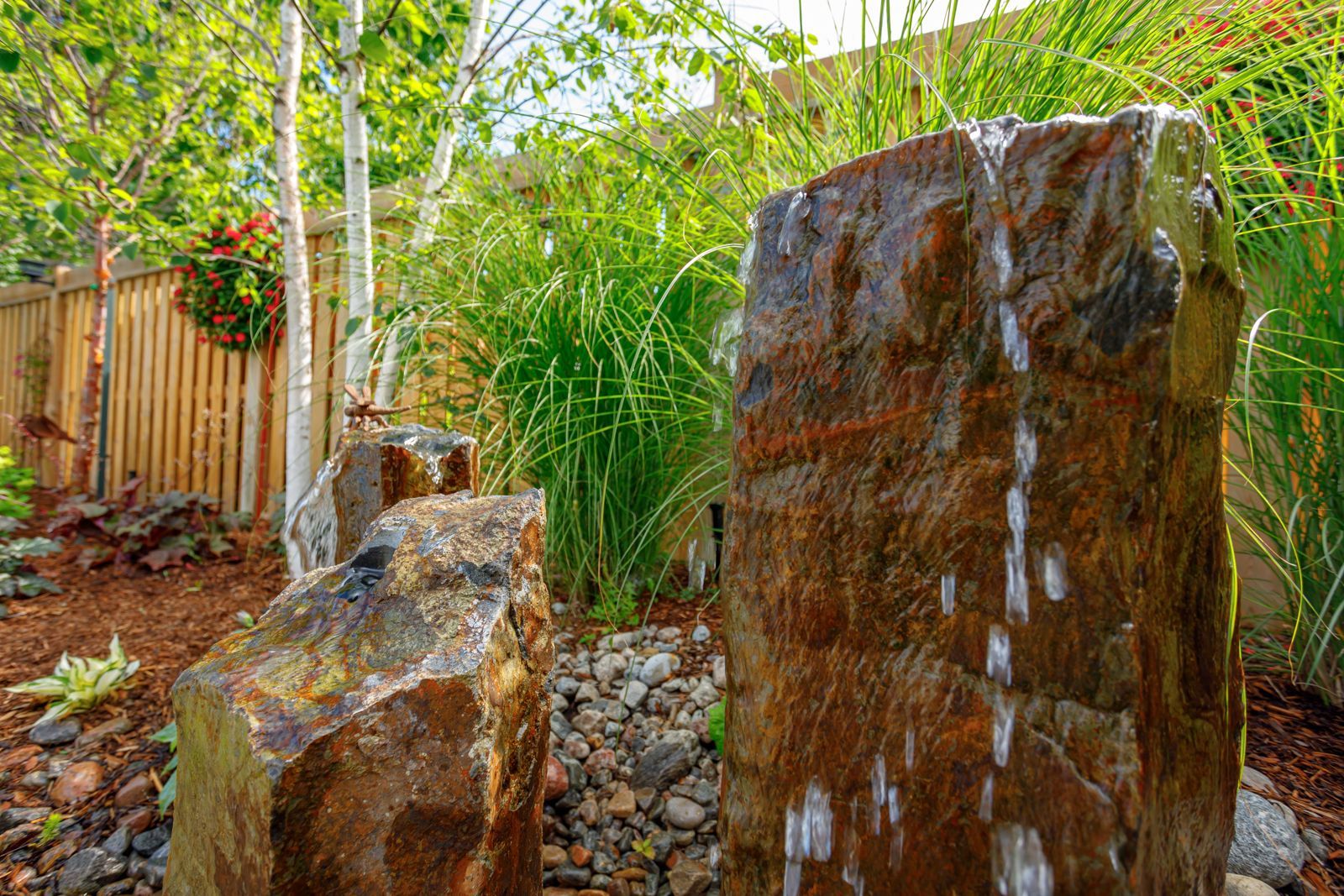 A water fountain is surrounded by rocks and trees in a backyard.