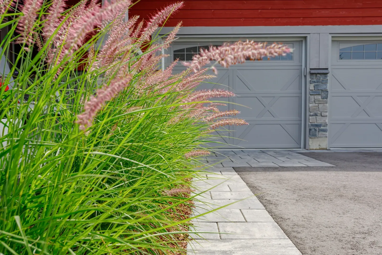 A red house with a gray garage door and flowers in front of it.