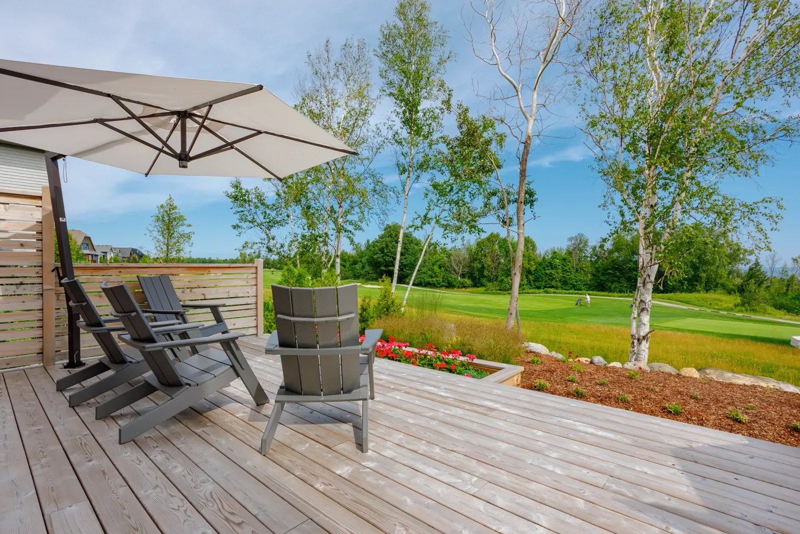 A wooden deck with chairs and an umbrella overlooking a golf course.