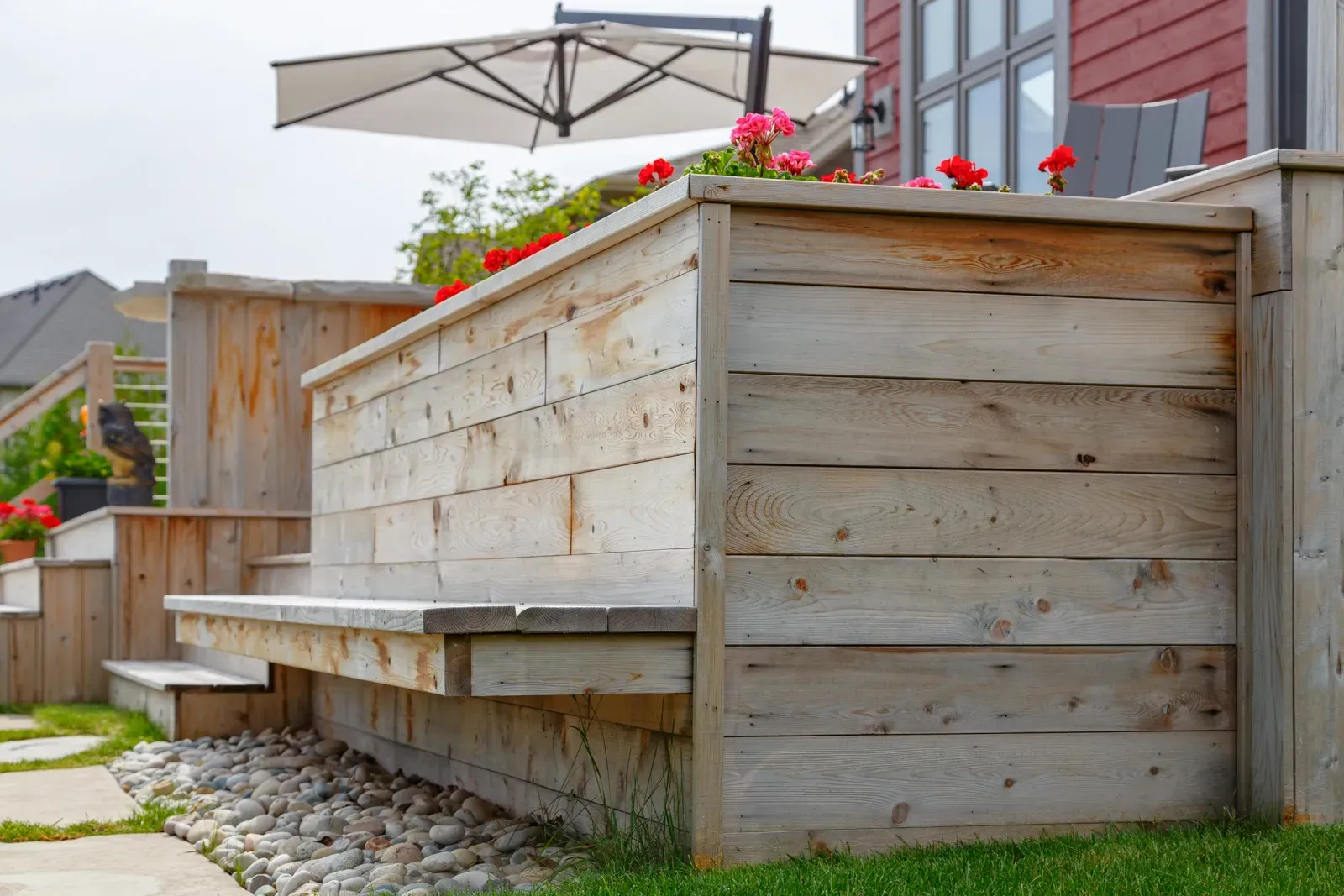 A wooden planter with flowers and an umbrella in a backyard.