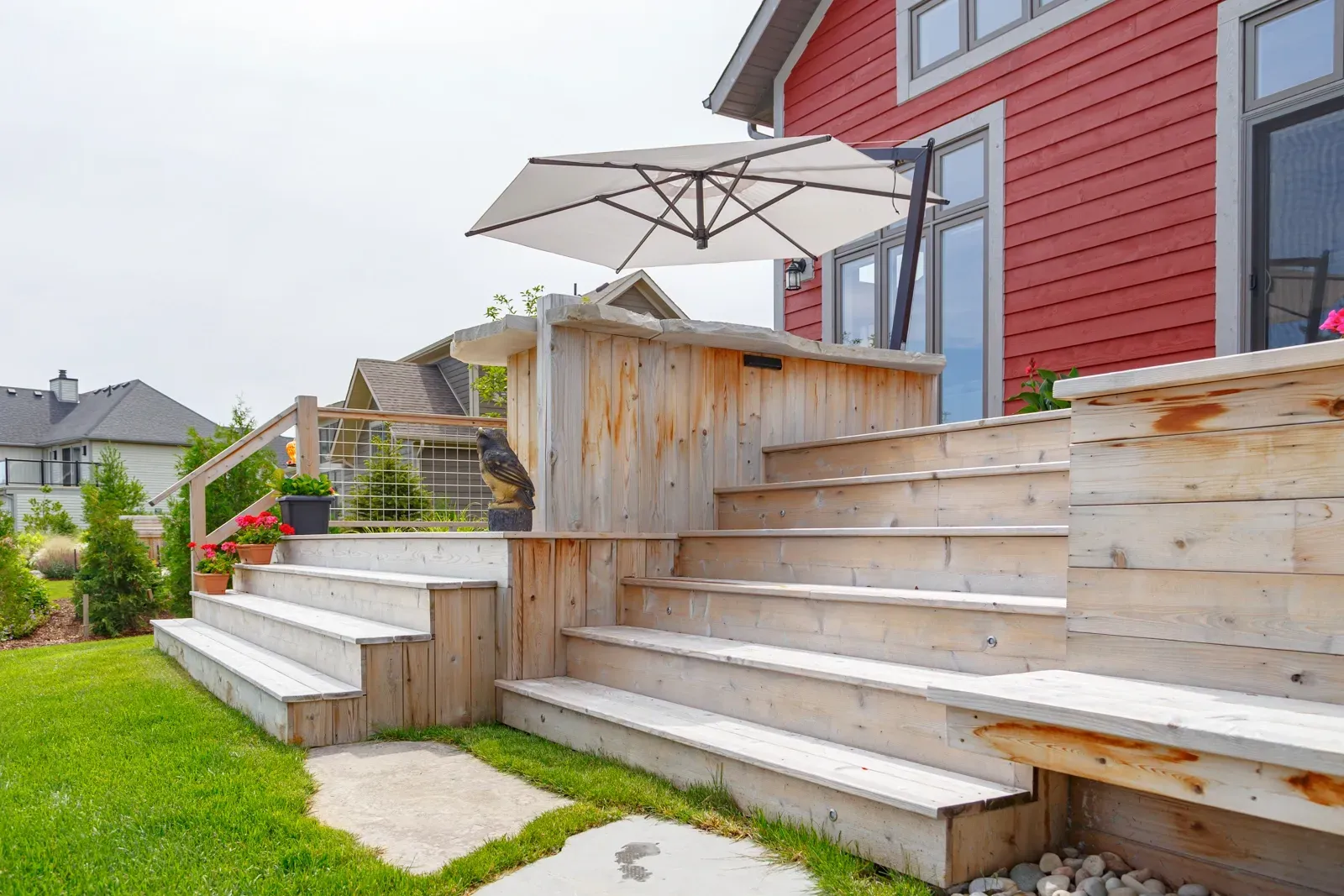 A wooden deck with stairs and an umbrella in front of a red house.