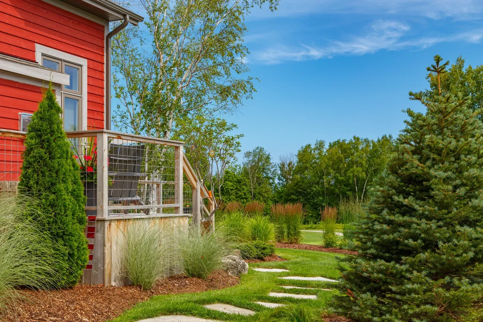 A red house with a deck and a walkway in front of it surrounded by trees.