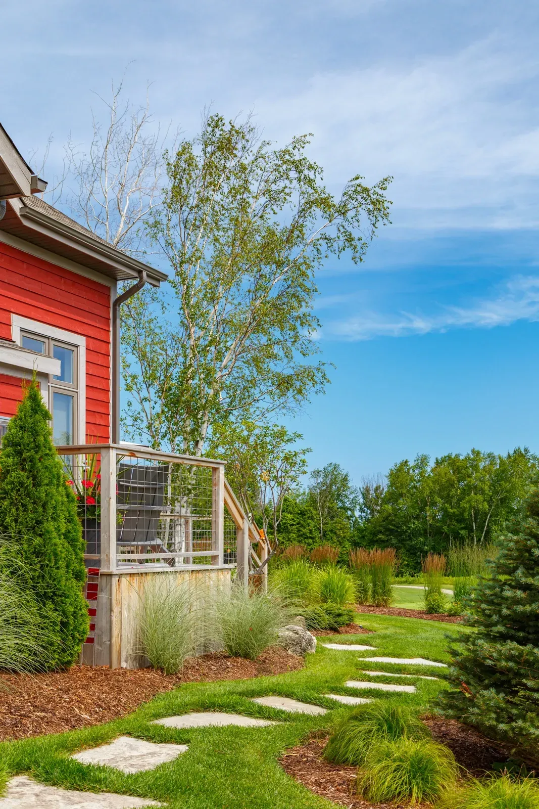 A red house with a walkway leading to it is surrounded by trees and grass.