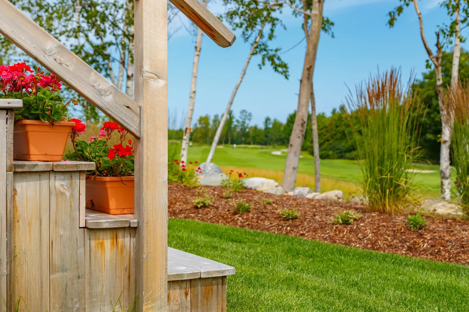 A wooden staircase with flowers in pots on the steps and a golf course in the background.
