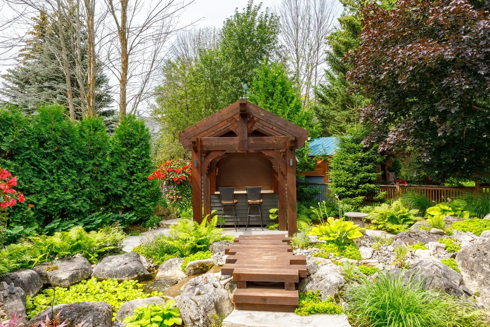 A wooden gazebo in the middle of a garden with a wooden walkway leading to it.