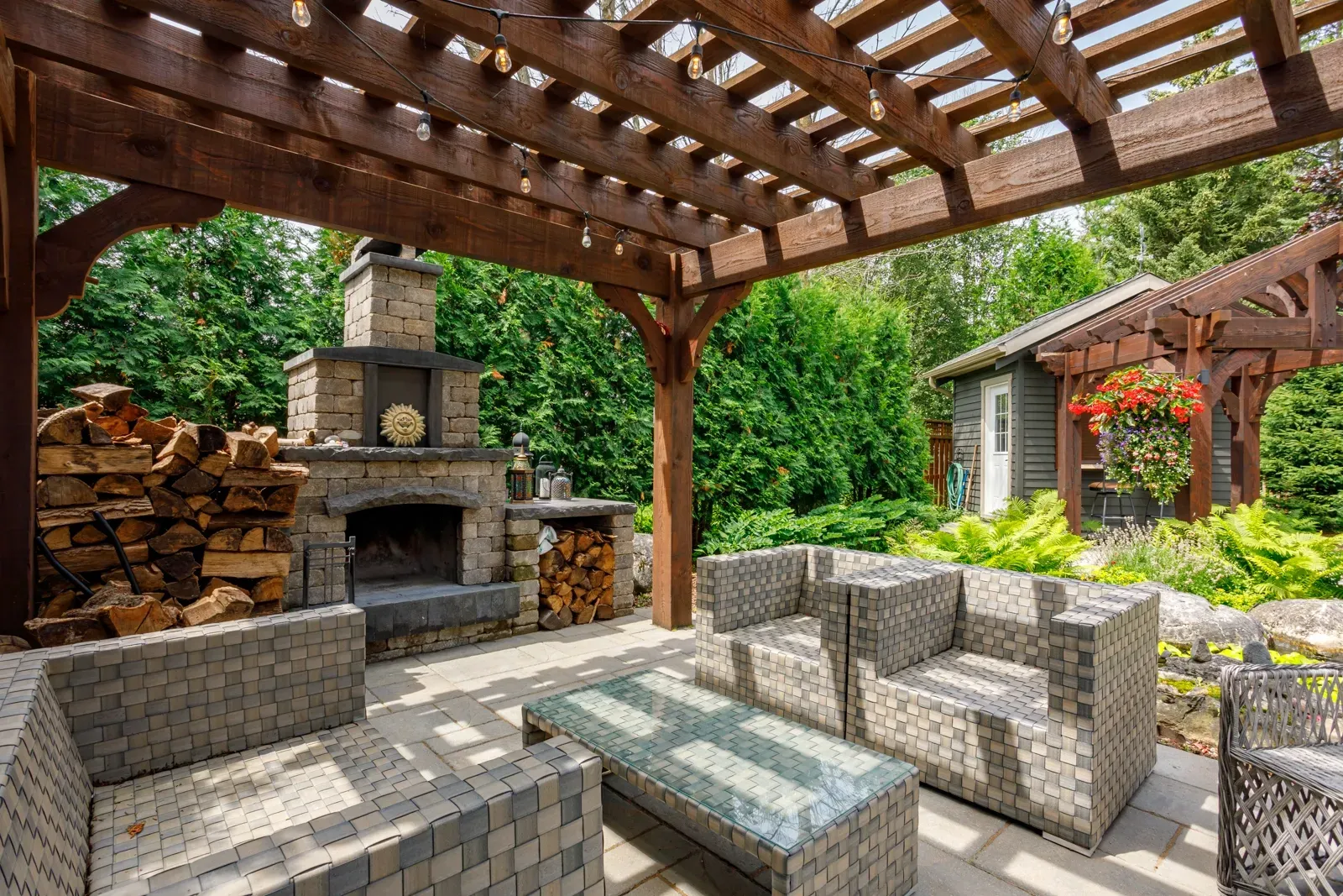 A patio with furniture and a fireplace under a pergola.
