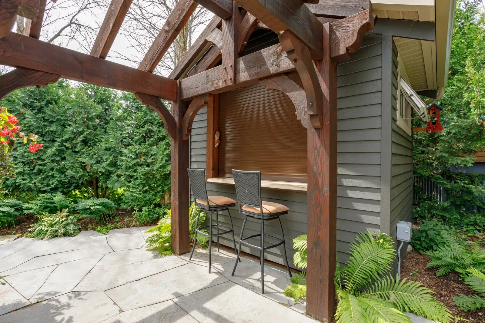 A wooden gazebo with a bar and stools underneath it.
