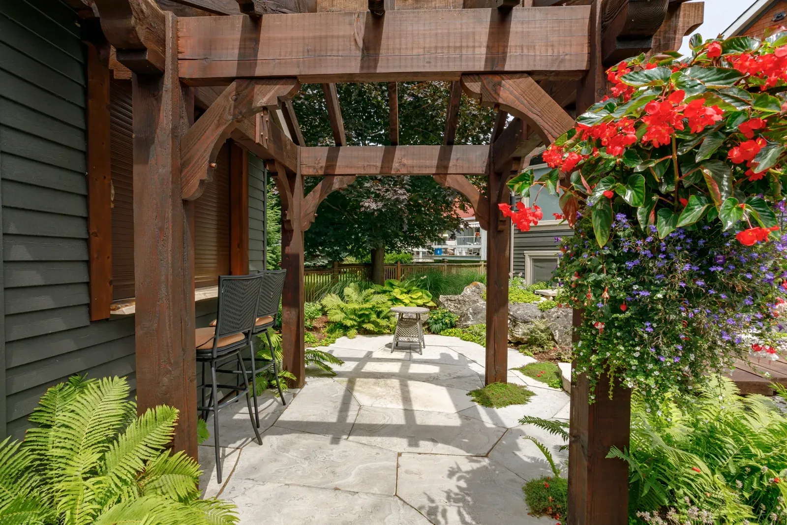 A wooden pergola is surrounded by flowers and ferns in a garden.