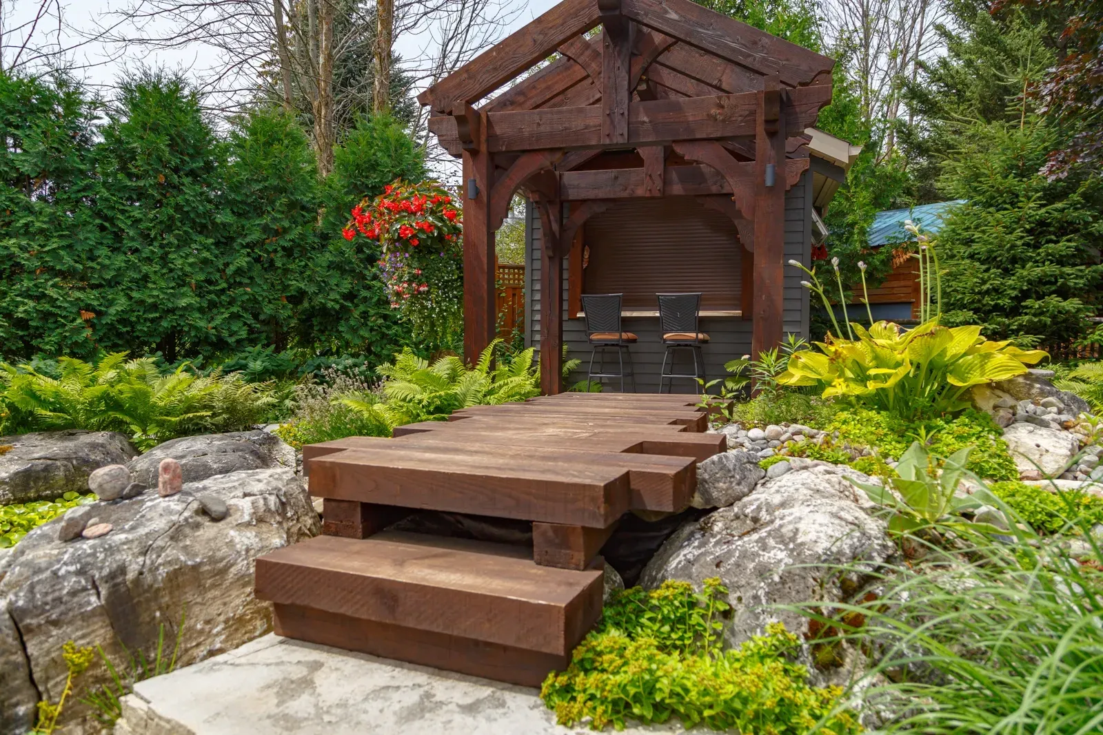 A wooden gazebo with stairs leading to it in a garden.