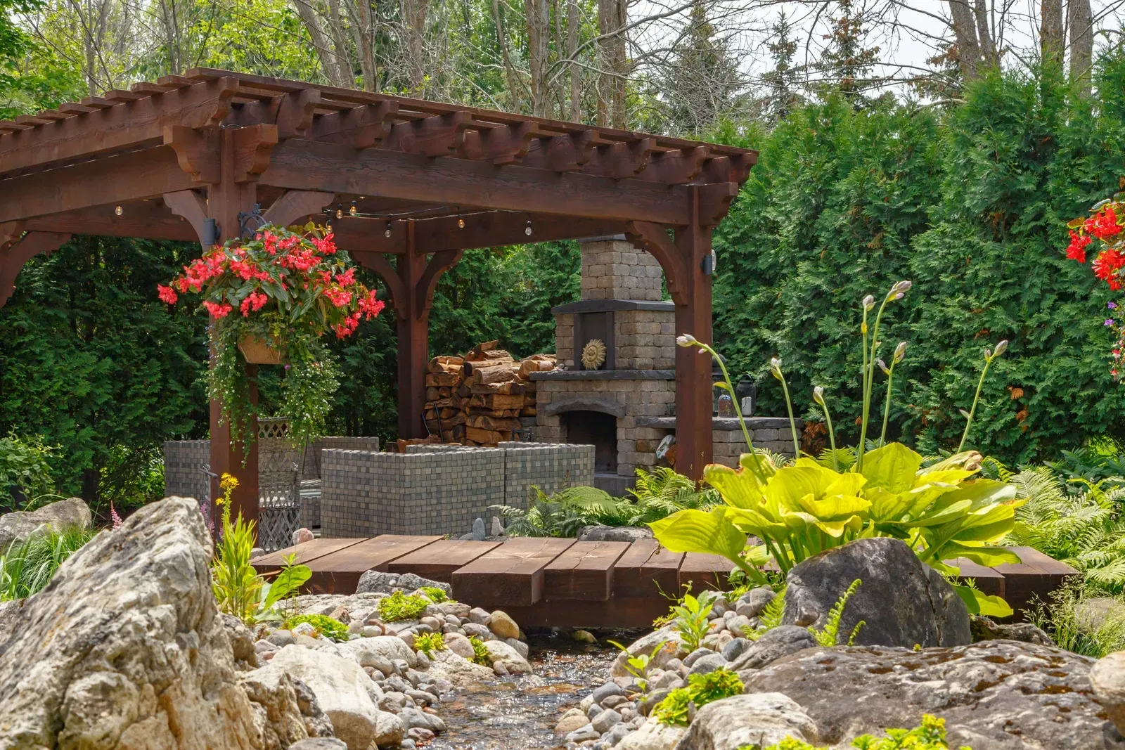 A wooden pergola with red flowers hanging from it in a garden.