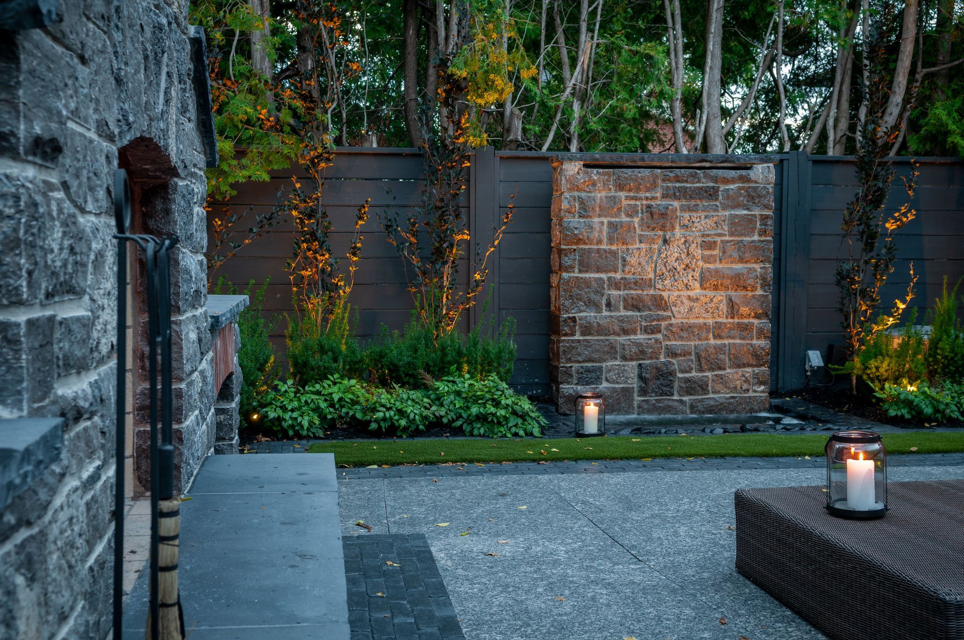 A backyard with a brick wall and a few candles on the ground.