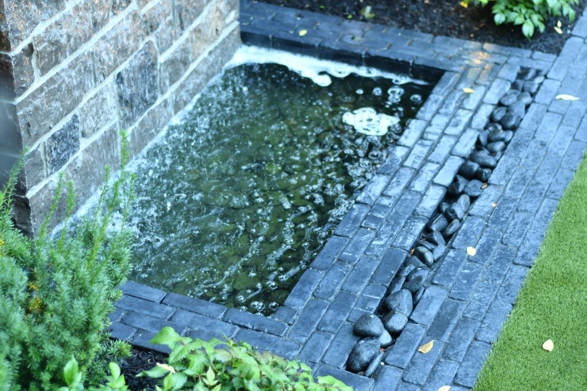 A small pond is surrounded by bricks and rocks in a garden.
