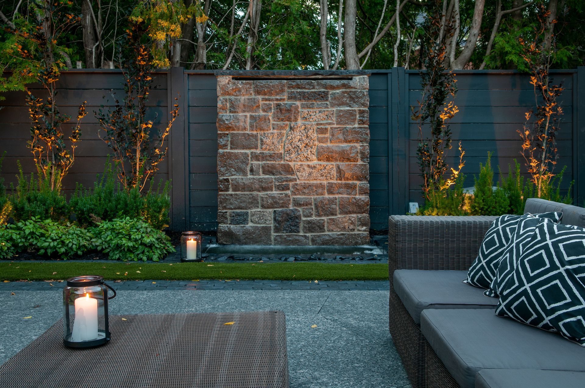 There is a waterfall in the backyard with a couch and a table.