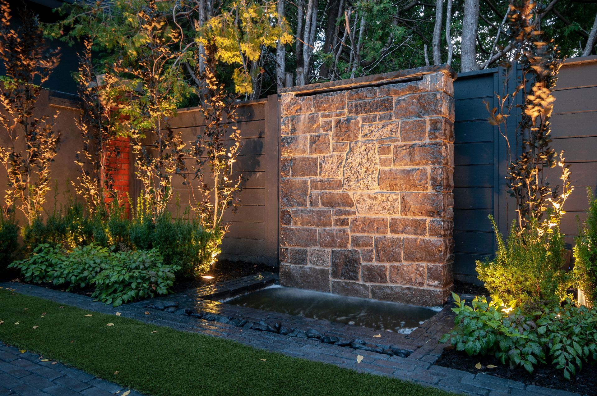 A brick wall with a waterfall in the middle of a garden.