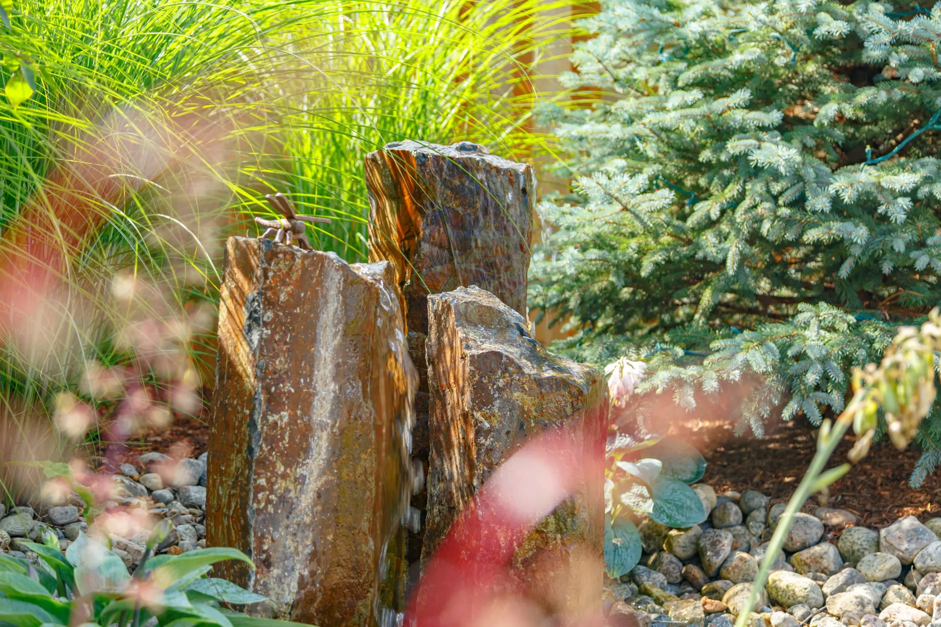 A fountain made of rocks in a garden with trees in the background.