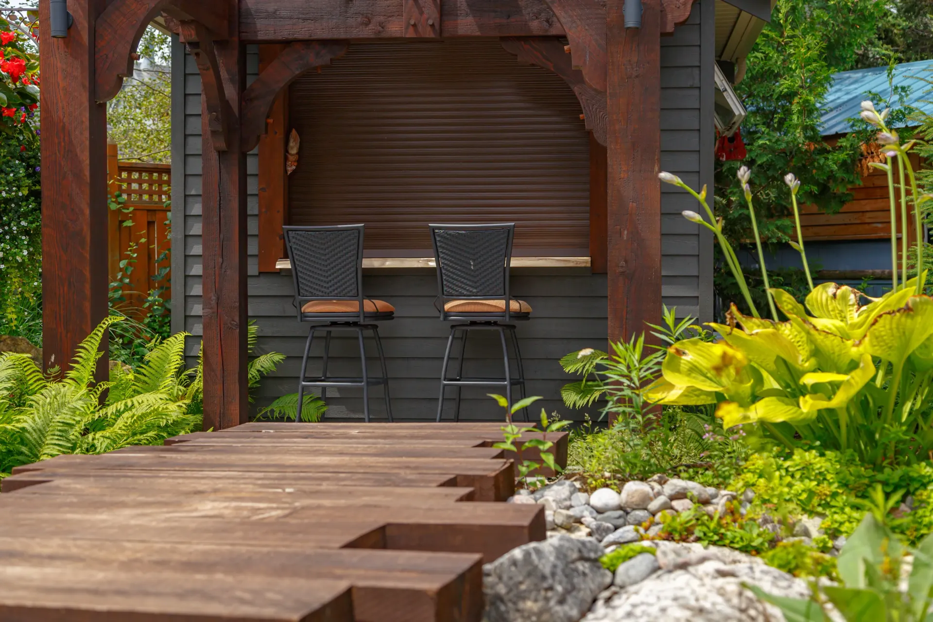 A wooden deck with two chairs under a pergola in a garden.