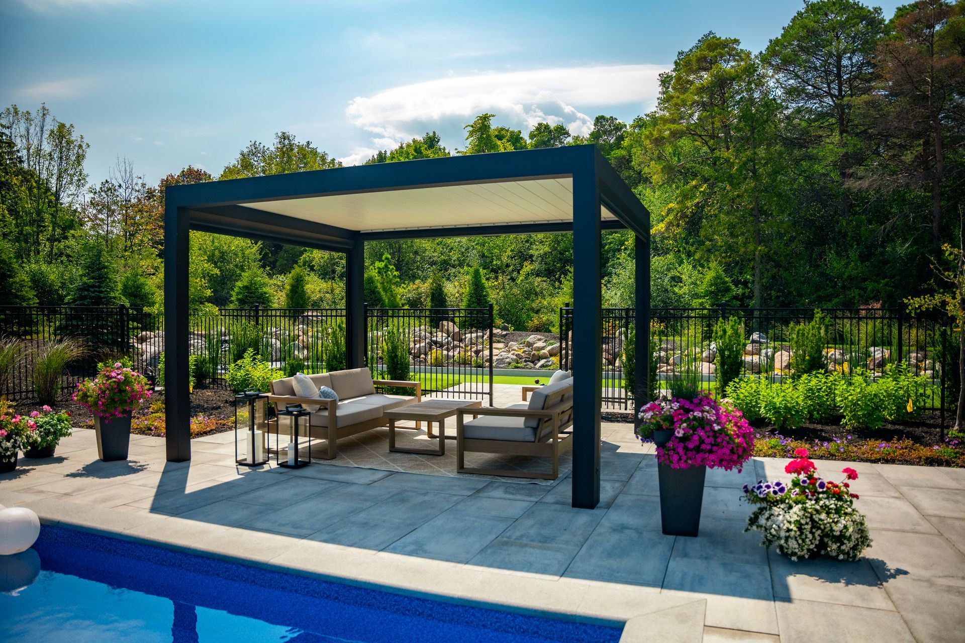 A patio with a pergola and a swimming pool in the background.