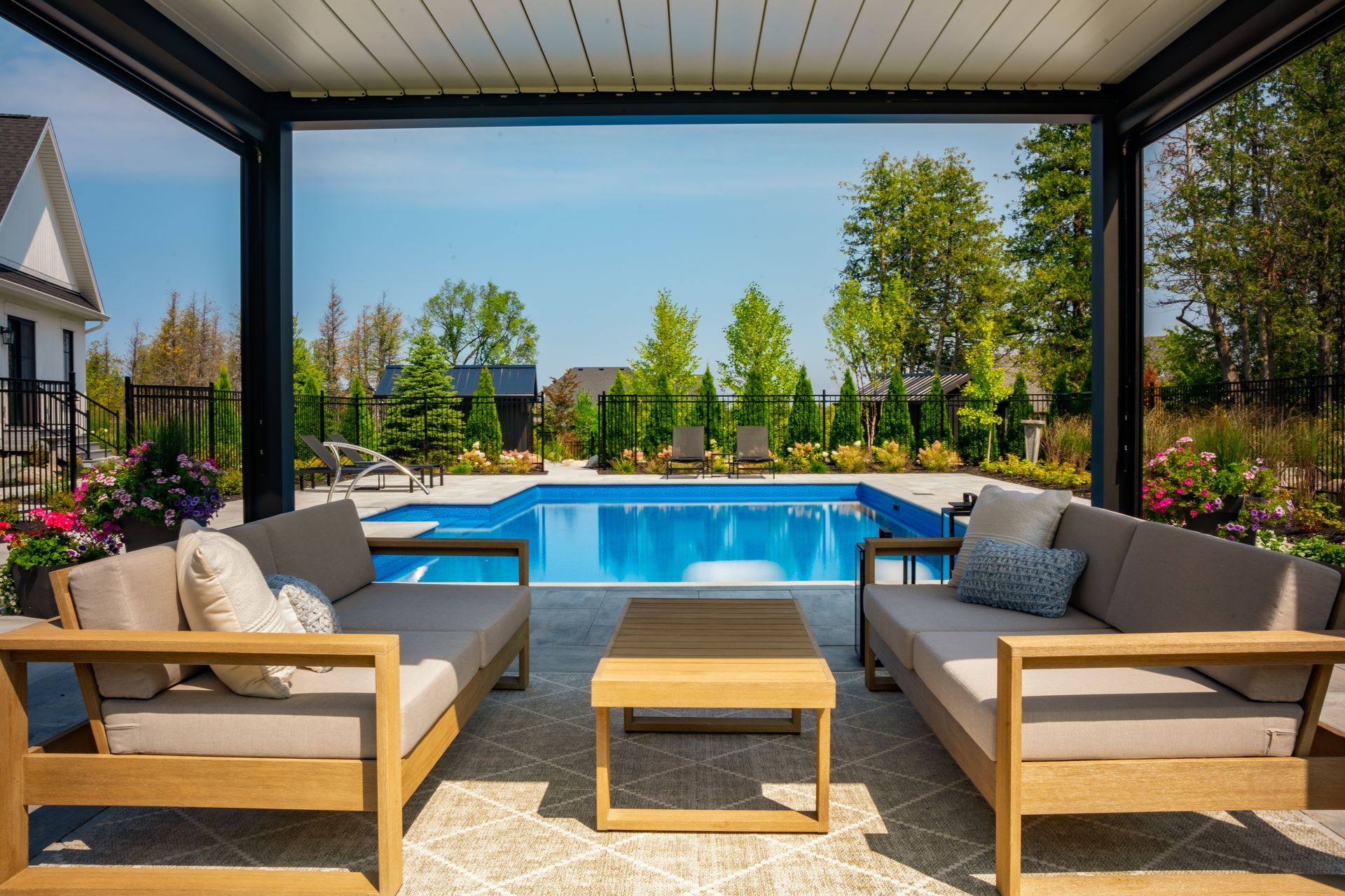 A patio with a couch , chairs , table and a pool in the background.