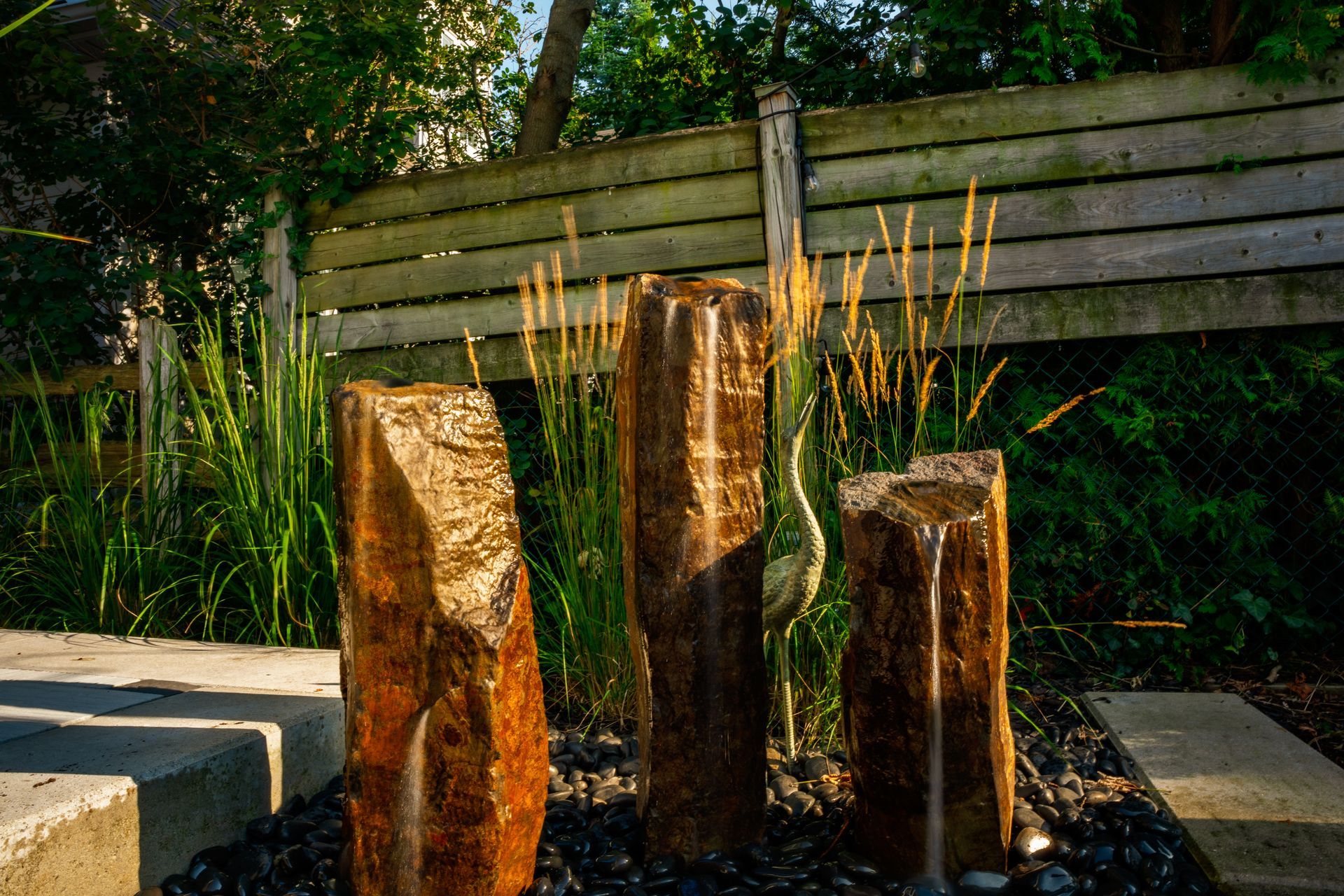 A fountain made of rocks in a garden with a wooden fence in the background.
