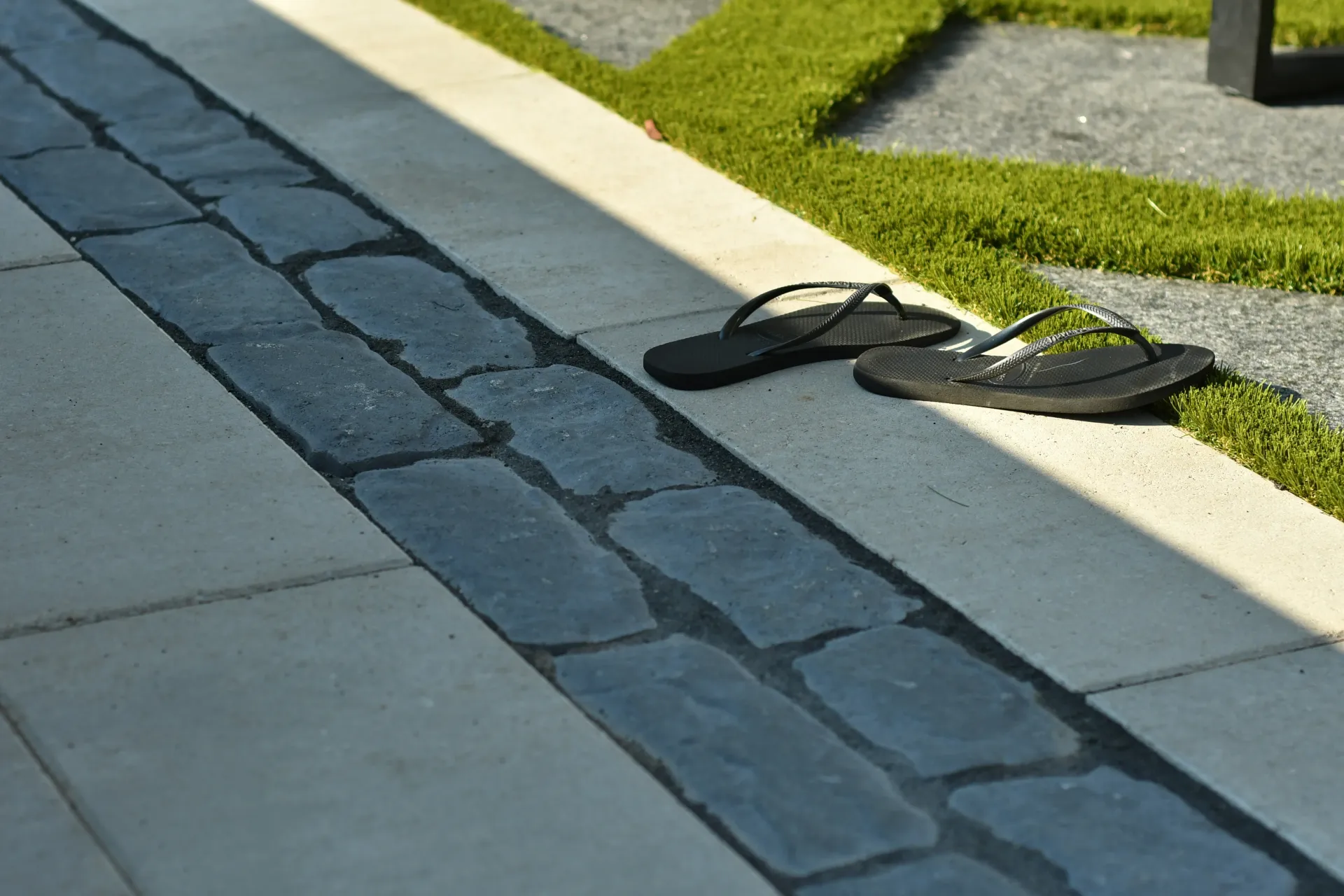 A pair of flip flops are sitting on a sidewalk next to a grassy area.