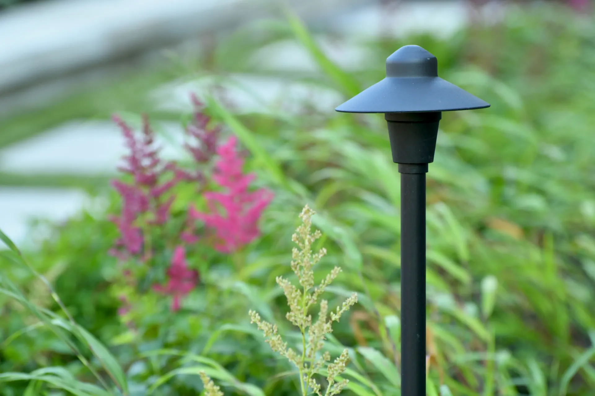 A black pole light is sitting in the middle of a garden.