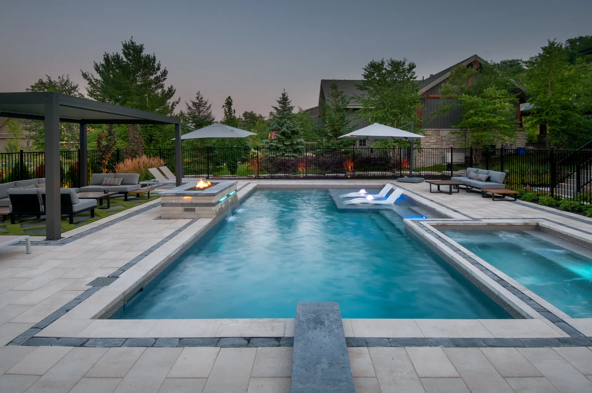 A large swimming pool surrounded by chairs and umbrellas in a backyard.
