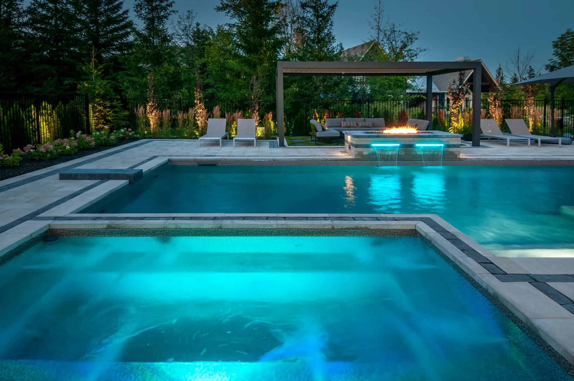 A large swimming pool with a fire pit in the backyard at night.