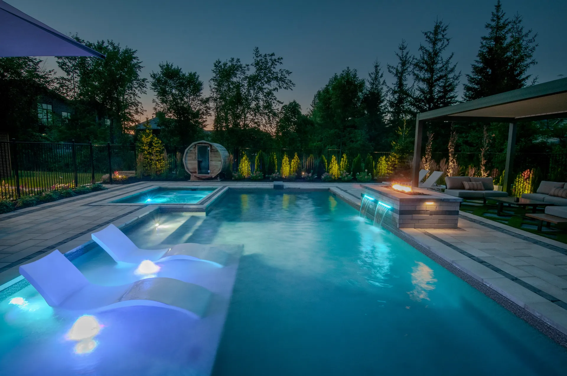 A large swimming pool is lit up at night in a backyard.
