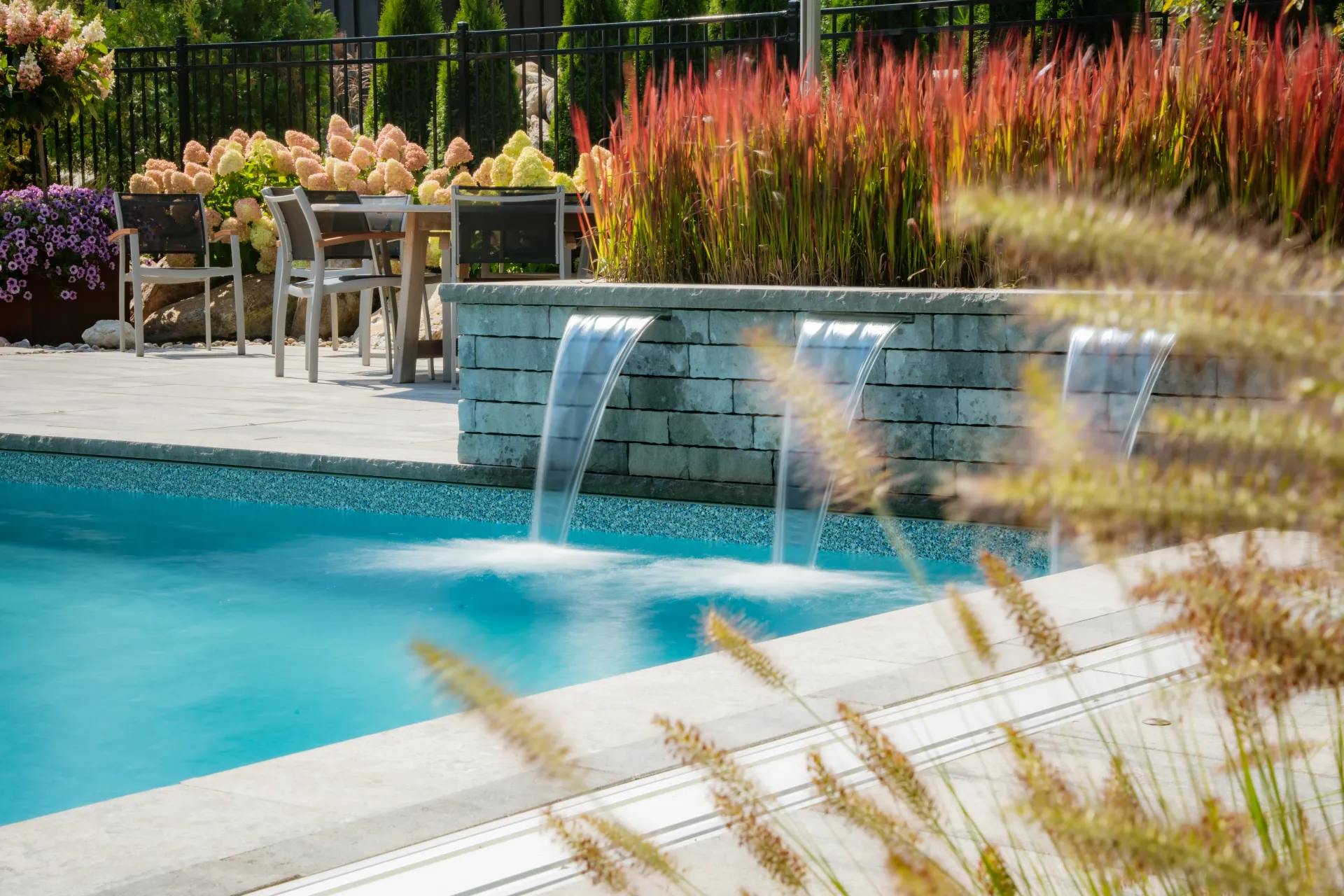 A swimming pool with a waterfall and a table and chairs in the background.