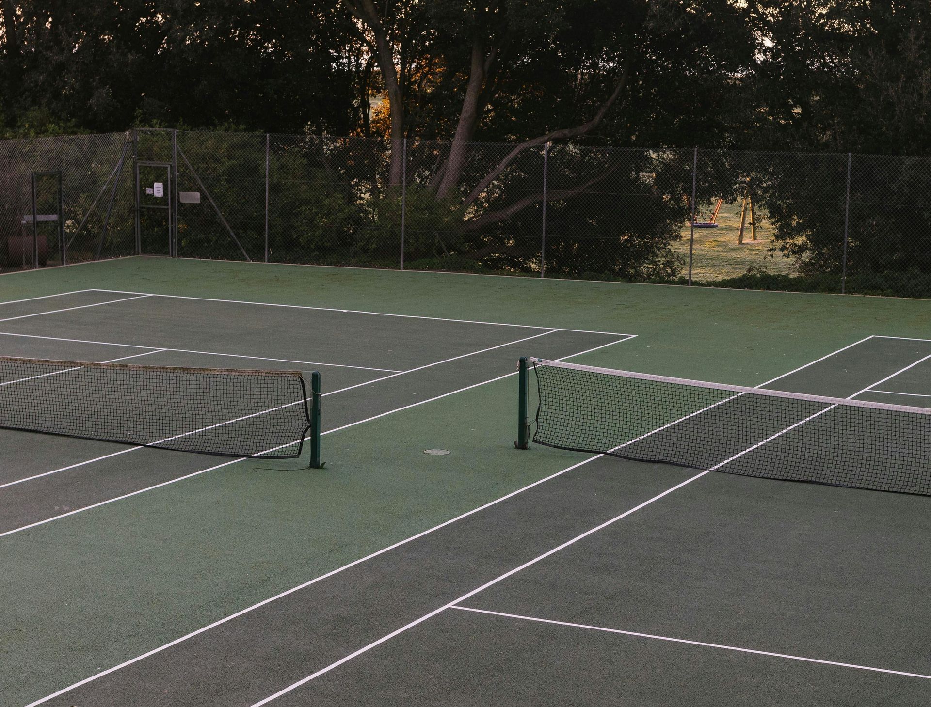 A tennis court with a fence and trees in the background