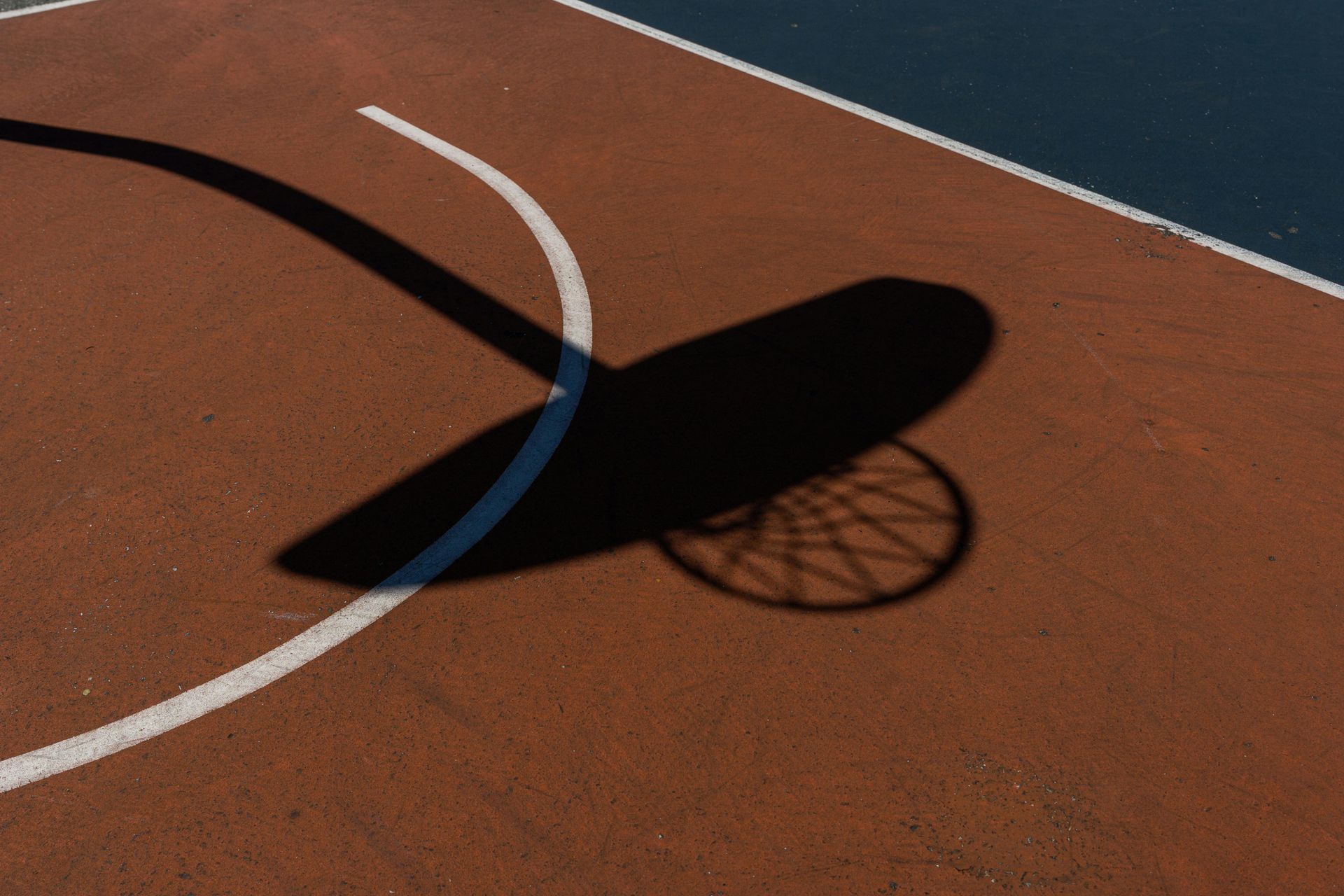 A shadow of a basketball hoop is cast on a basketball court