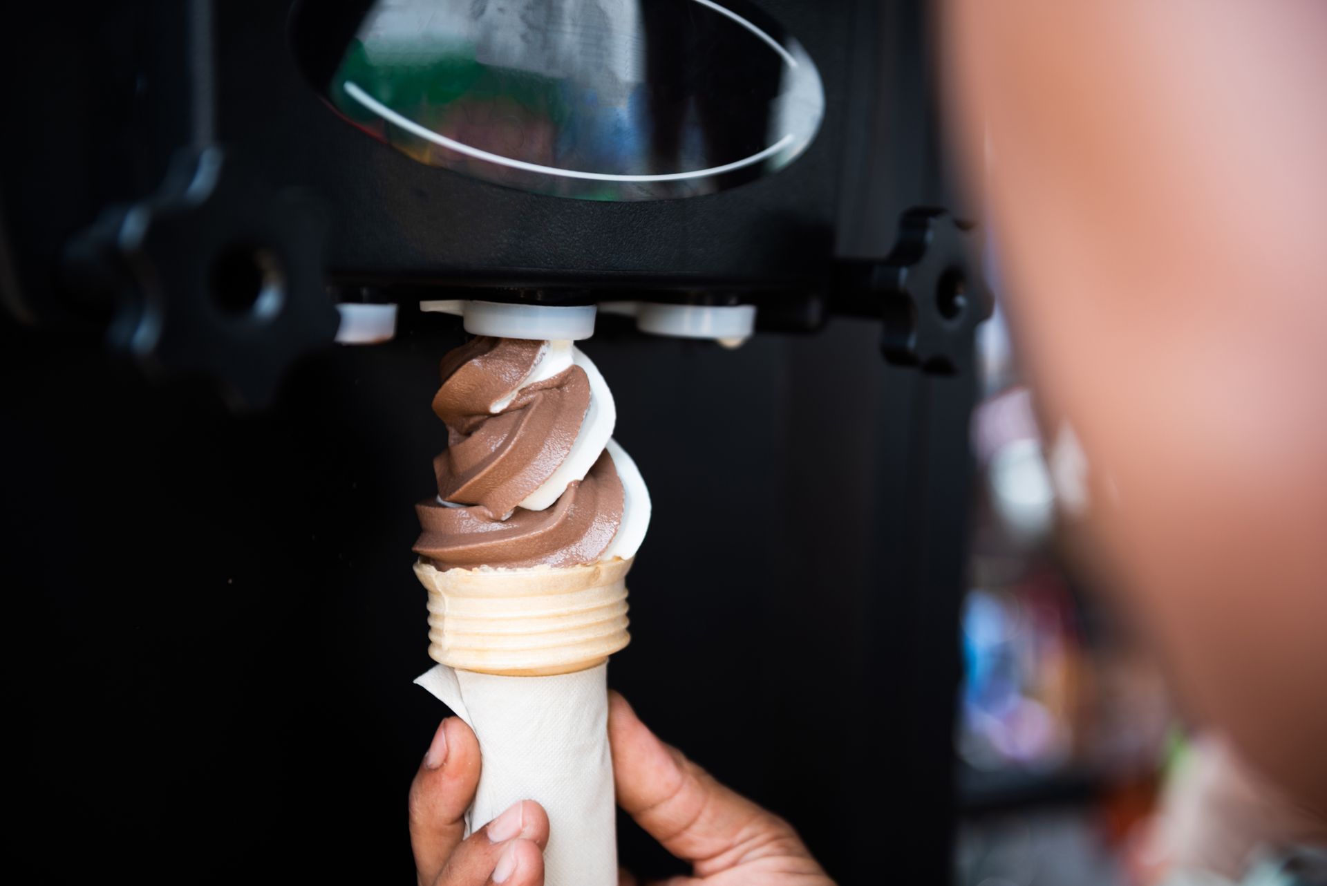 Une main tient une spirale de glace molle au chocolat et à la vanille qui sort d'une machine.