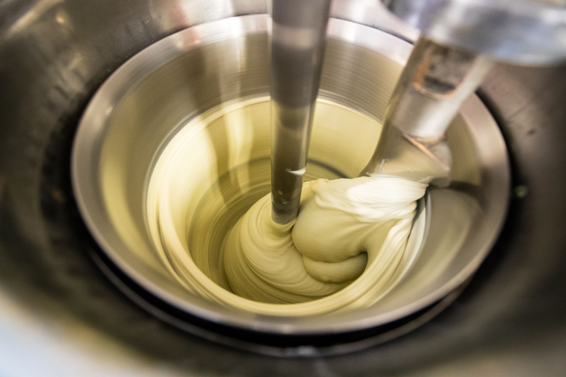 Un batteur industriel argenté mélangeant une crème épaisse et pâle dans un bol en acier inoxydable.