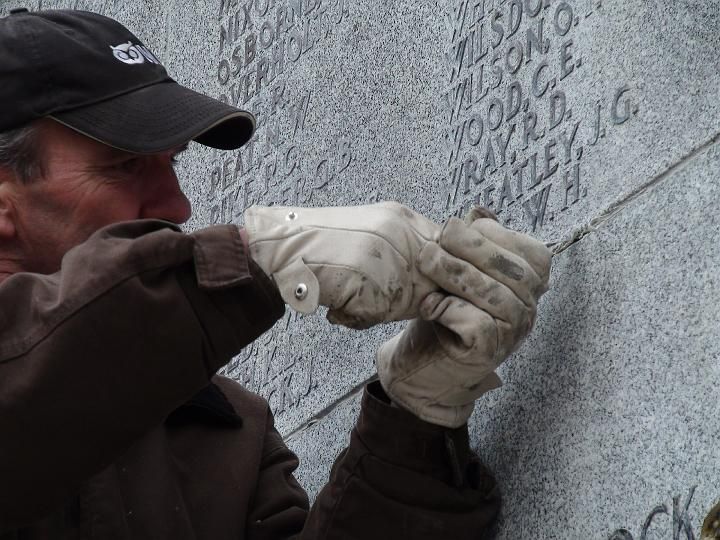 a man wearing a hat and gloves is working on a stone wall