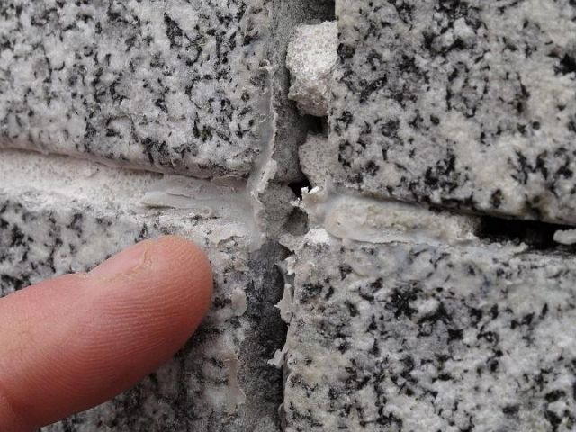 a person is pointing at a hole in a brick wall .