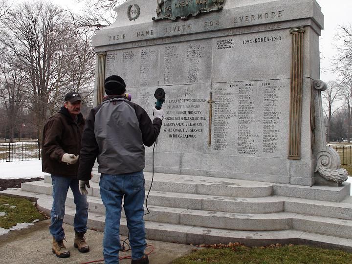 two men stand in front of a memorial that says 